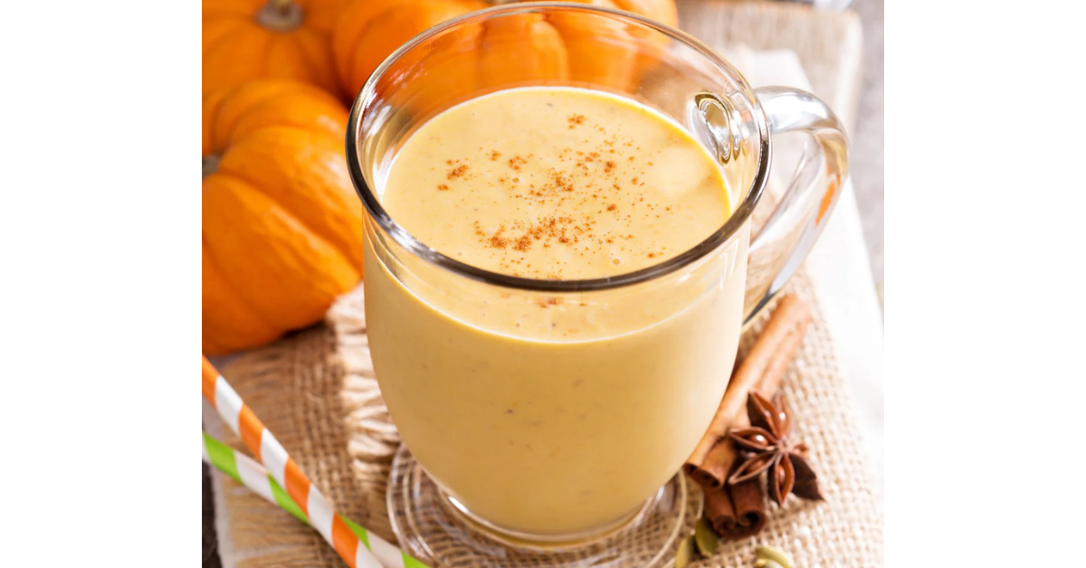 Inviting warm pumpkin smoothie with a dash of cinnamon on top. Mini pumpkins in the background.
