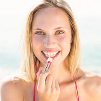 Holding Beessential Rose Mint Lip Balm on a beach. All-natural protection for sun-kissed, hydrated lips.