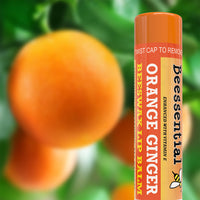 Beessential Orange Ginger Lip Balm tube placed next to fresh oranges on a tree, emphasizing its natural scent.
